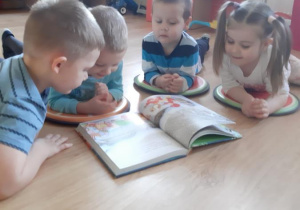Szymek, Miłosz, Adaś i Zosia oglądają książkę z bajkami.